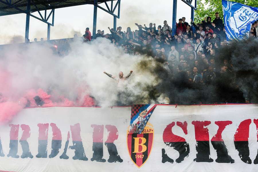 Torcedores do FK Vardar gesticulam enquanto a fumaça sai da arquibancada durante uma partida de futebol da segunda divisão da Macedônia do Norte