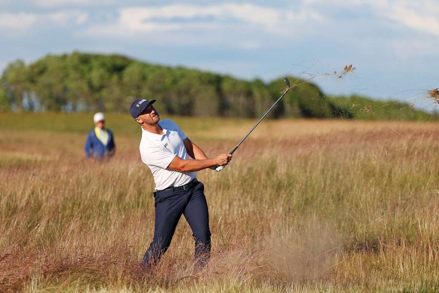 Wyndham Clark hits a shot out of the high grass on the 13th fairway