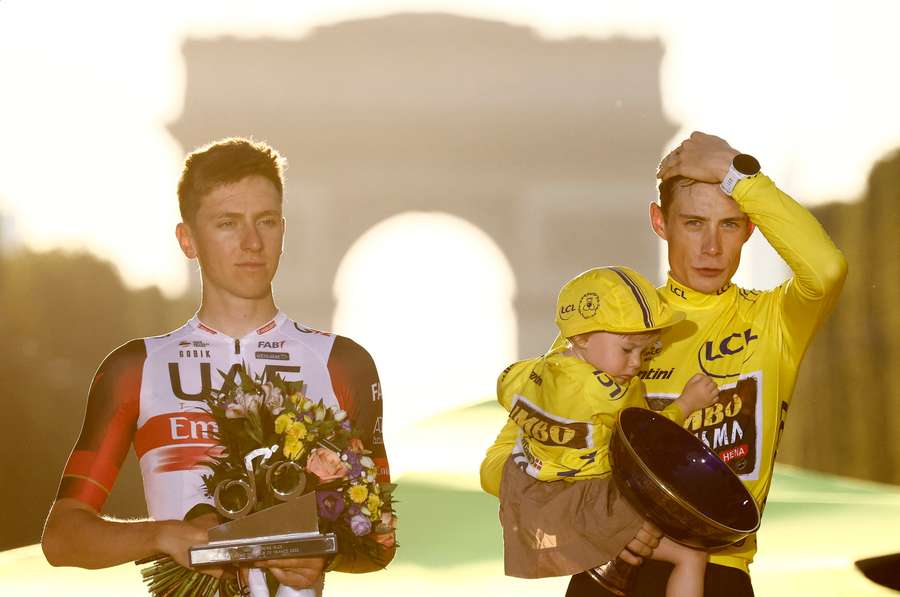 Vingegaard celebrates with the trophy, wearing the overall leader's yellow jersey, after winning the Tour de France in 2022 next to Pogacar