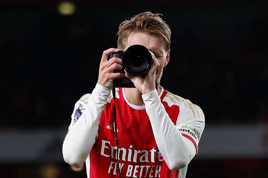 Arsenal midfielder Martin Odegaard picks up a camera and takes pictures as he celebrates