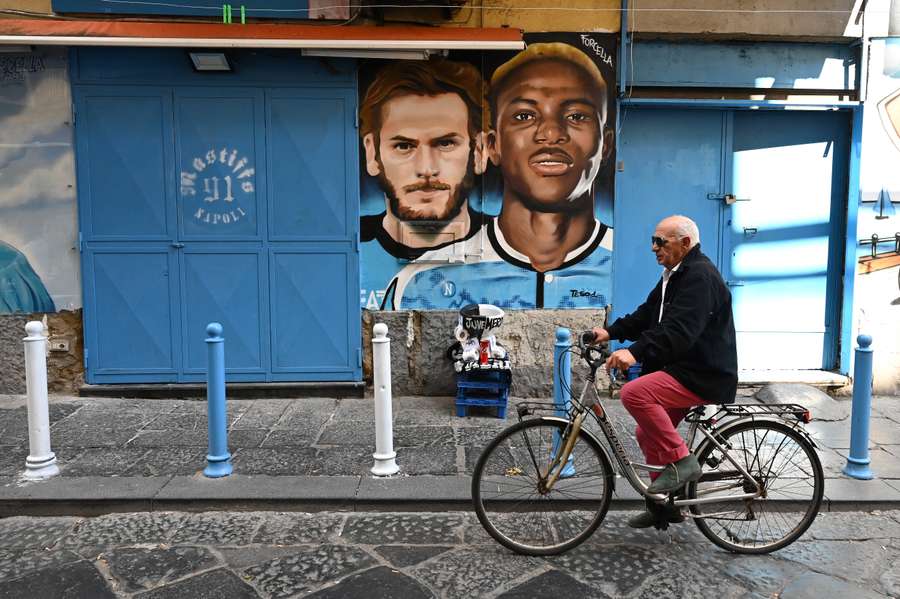 A man cycles past a mural depicting Napoli's Georgian forward Khvicha Kvaratskhelia and Nigerian forward Victor Osimhen