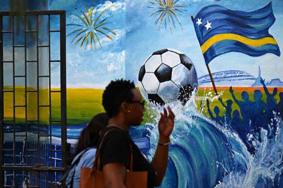 Women walk past a mural depicting a football and a flag of Curaçao in Willemstad