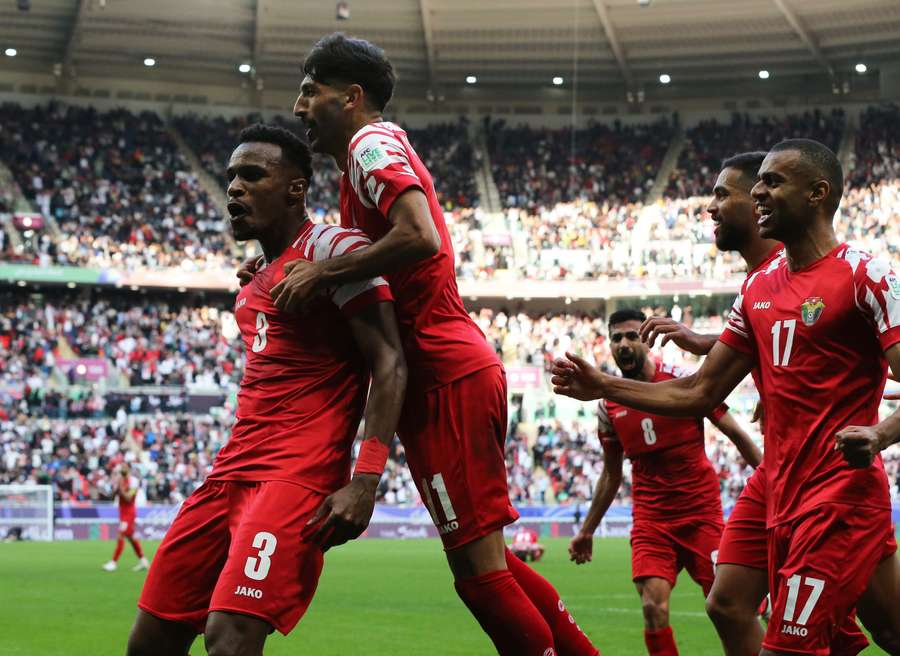 Jordan's Abdallah Nasib celebrates with teammates after Tajikistan's Vakhdat Khanonov scores an own goal