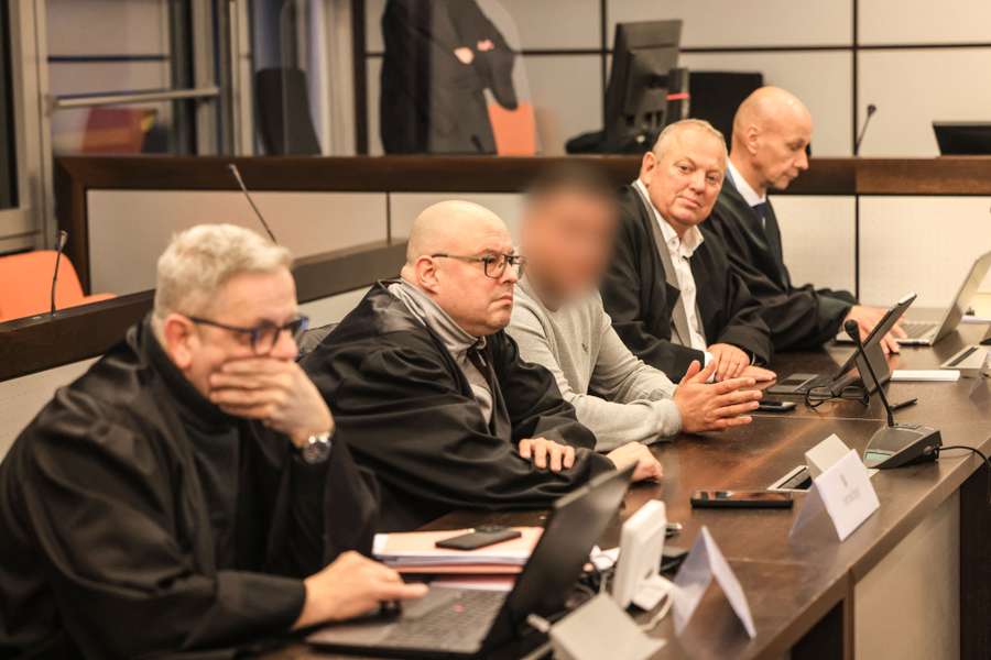 One of the three defendants (blurred) sits between lawyers in the courtroom of the district court before the verdict is announced