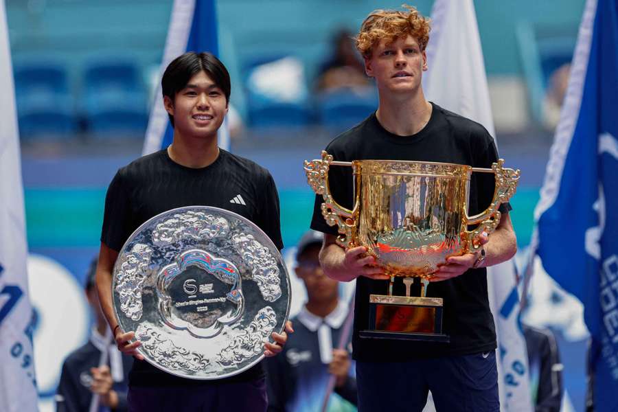 Jannik Sinner (R) holds the winner's trophy