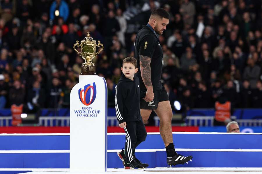 O hooker neozelandês Codie Taylor (R) segura a mão de uma criança que olha para a Taça Web Ellis depois de a África do Sul ter ganho o Campeonato do Mundo de Rugby França 2023