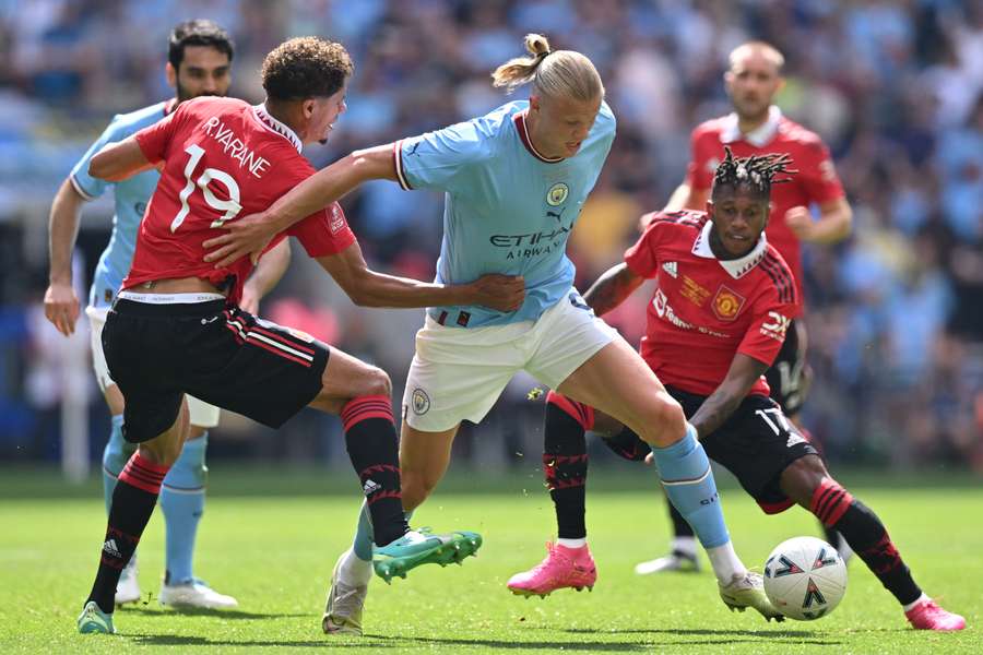 Manchester City striker Erling Haaland (C) vies with Manchester United midfielder Fred (R) and defender Raphael Varane (L)