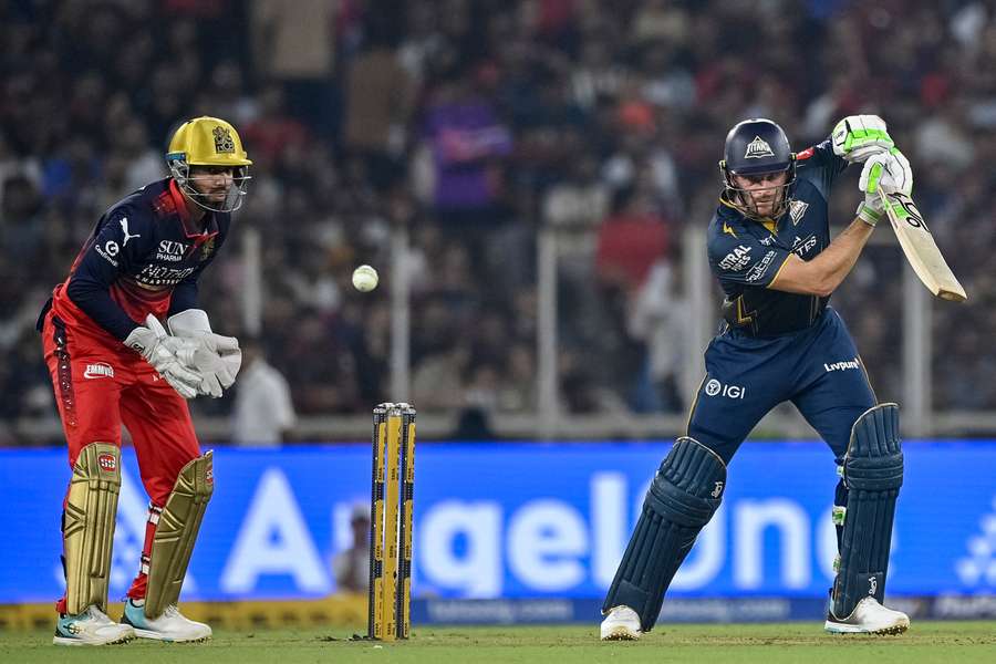 Gujarat Titans' Jos Buttler (right) plays a shot as Royal Challengers Bengaluru's Jitesh Sharma watches on