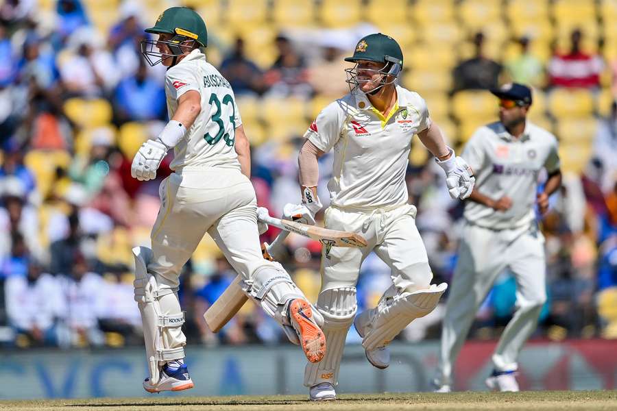 Australia's Marnus Labuschagne (L) and teammate David Warner (C) run between the wickets