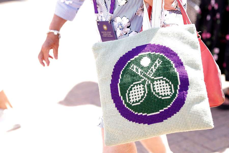 Spectator goes past with a crochet Wimbledon logo bag