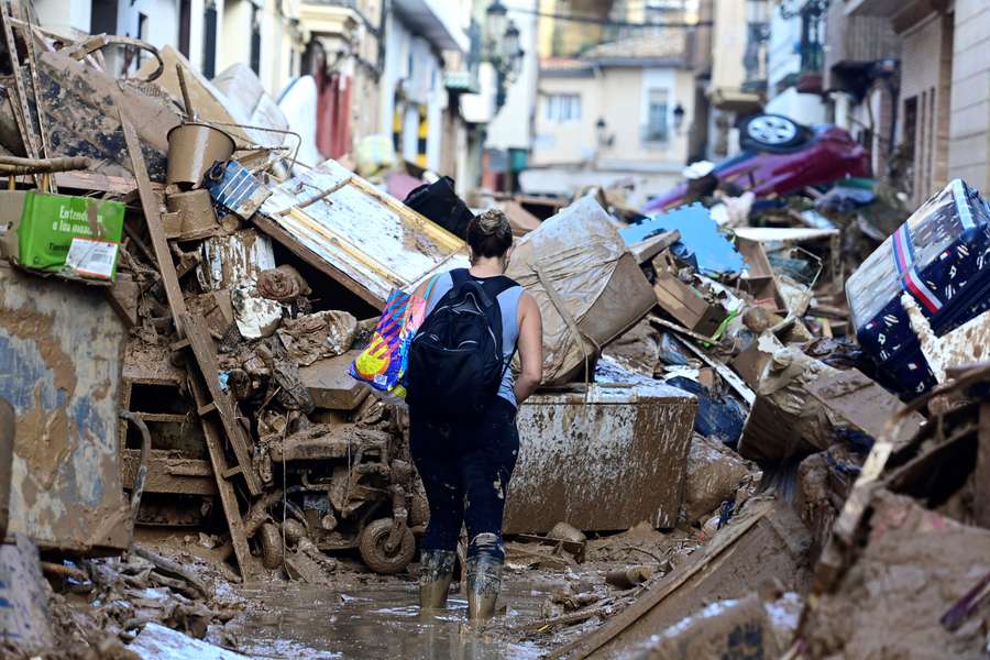 A resident walks down a street blocked by debris and piled up cars in Paiporta, in the region of Valencia, on Monday