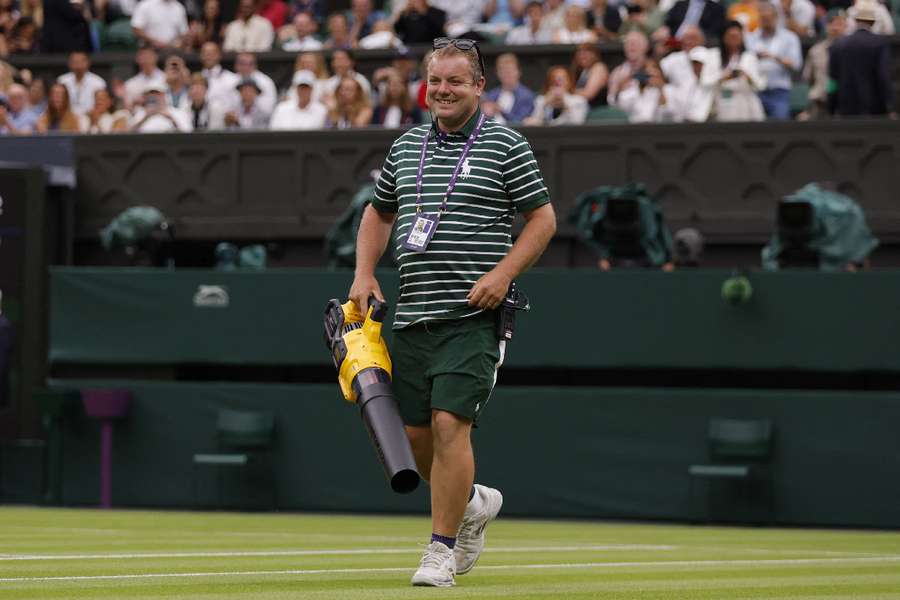 A member of groundstaff holds a leaf blower as they attempt to dry the court