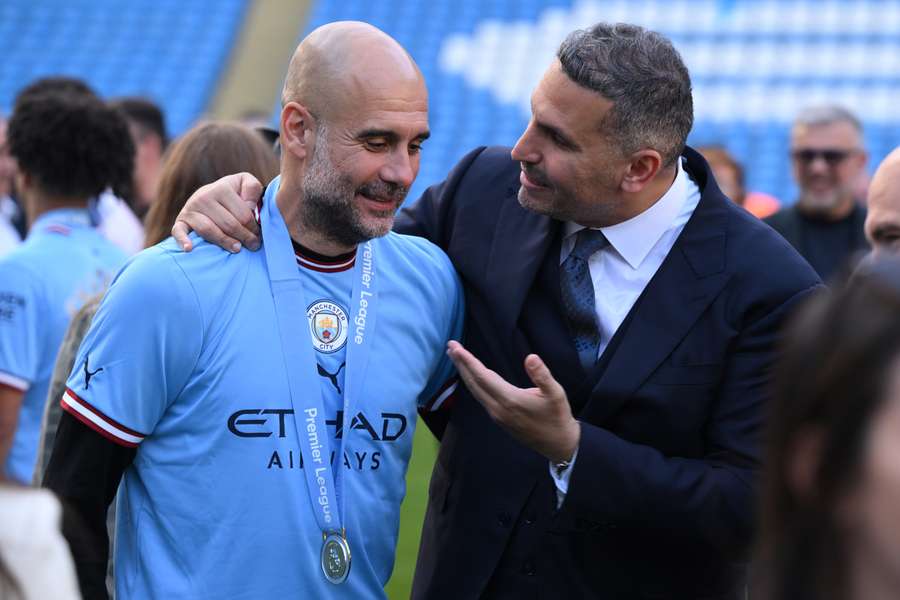 Pep Guardiola (esq.), técnico espanhol do Manchester City, conversa com Khaldoon al-Mubarak (dir.), presidente do Manchester City dos Emirados Árabes, no gramado após a cerimônia de entrega