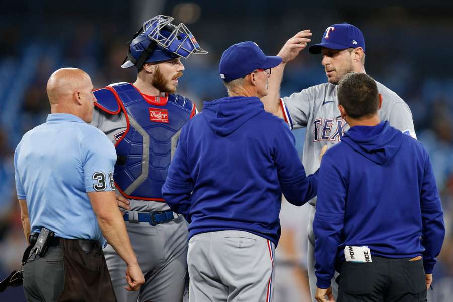 Max Scherzer of the Texas Rangers meets with trainers and coaches on the mound before leaving the game