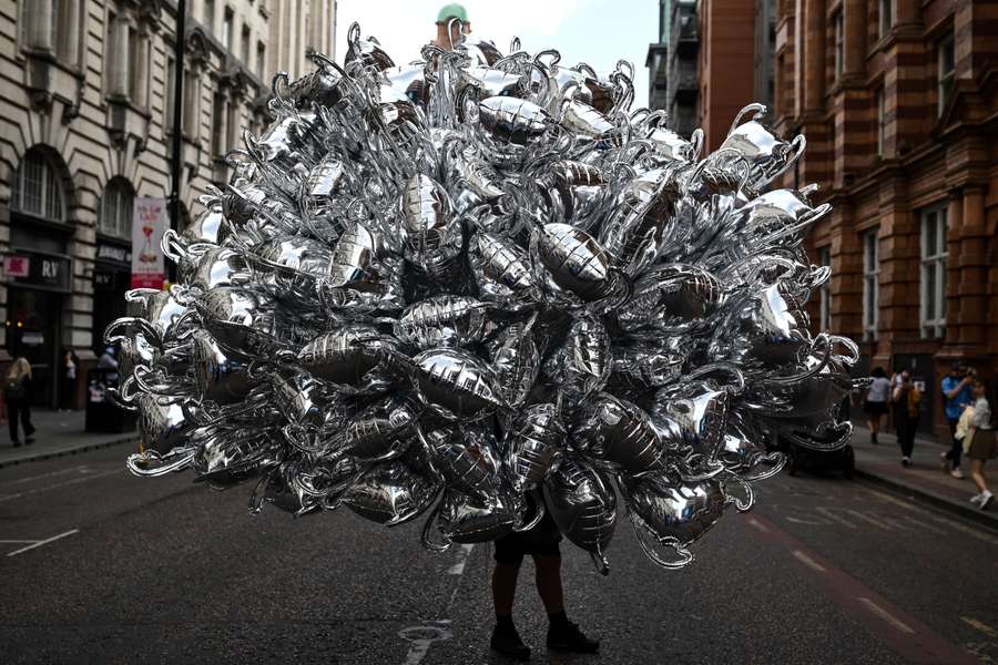 A balloon seller carries inflatable trophies ahead of Man City's victory parade