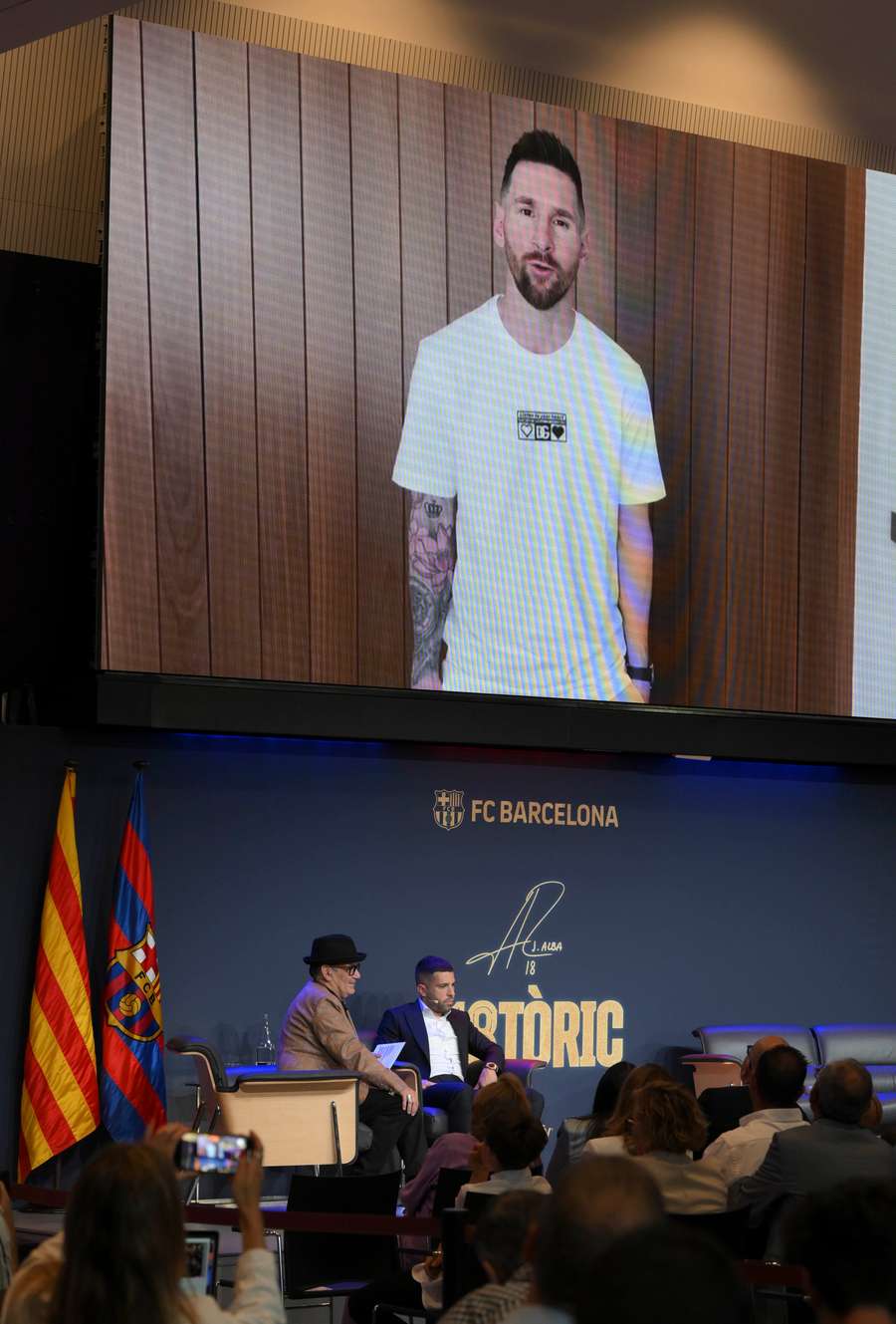 Hiszpański obrońca Barcelony Jordi Alba (po prawej) słucha wiadomości od byłego zawodnika Barcelony Lionela Messiego (na ekranie) podczas pożegnalnej imprezy na Camp Nou.