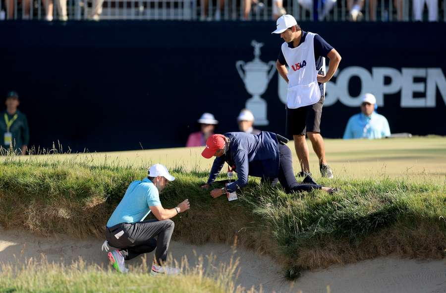 Rory McIlroy of Northern Ireland attempts to find his golf ball on the 14th hole which had embedded in the face of a green-side bunker