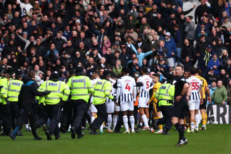 Jogadores do West Brom e do Wolves entre os agentes da polícia durante o incidente na multidão que levou à interrupção do jogo