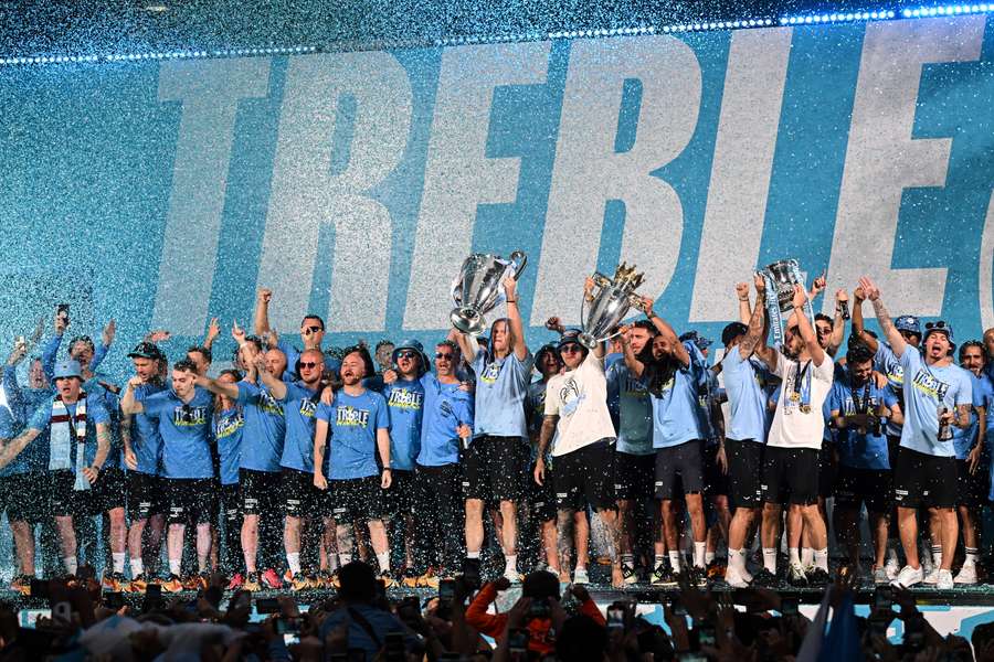 Man City celebrate with all three trophies on stage