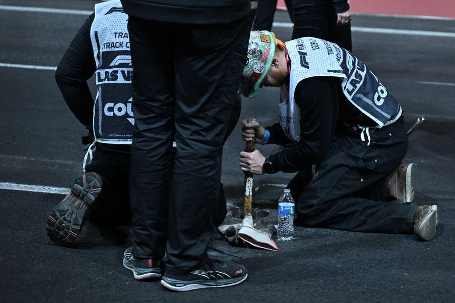 A work crew hammers in sand used to fill a drain hole on the track after trouble with the drain cover halted the first practice session