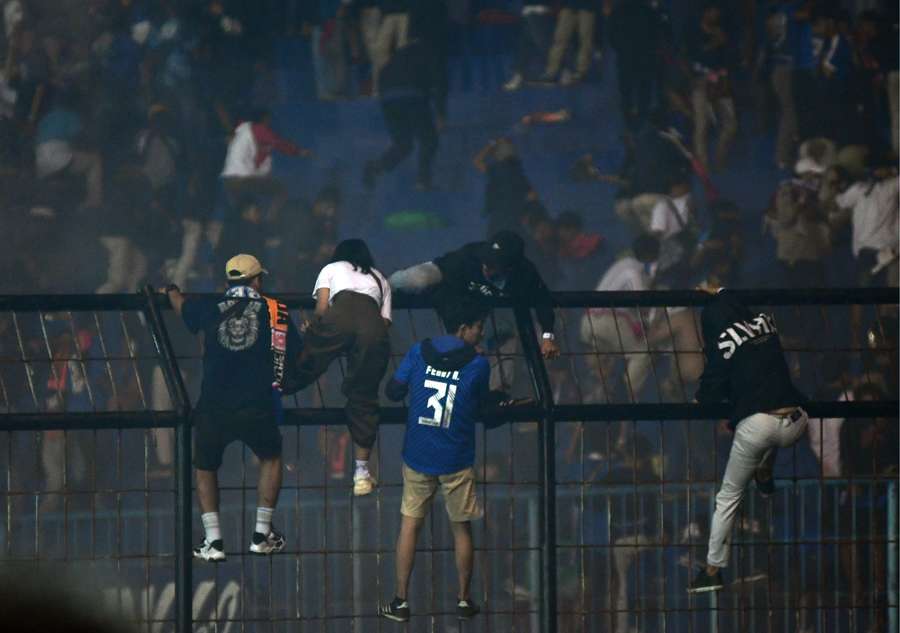 Spectators climb on a fence by the stands amid a deadly stampede at the Kanjuruhan stadium.