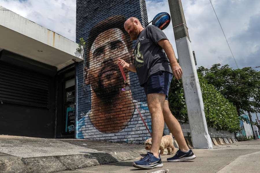 Um homem passeia com o seu cão junto a um mural de Messi em Miami.