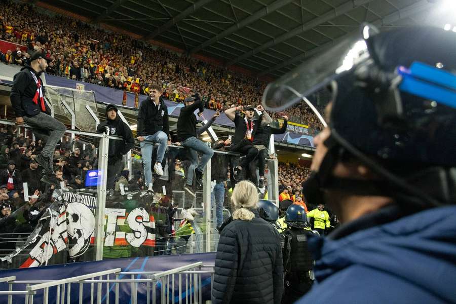 Supporters van PSV klimmen op de hekken onder toeziend oog van een ME'er