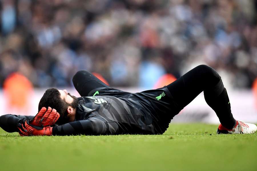 Alisson Becker ligt geblesseerd op het gras tijdens de wedstrijd tegen City