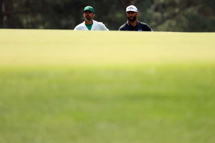 Jon Rahm and his caddie Adam Hayes look on from the third green