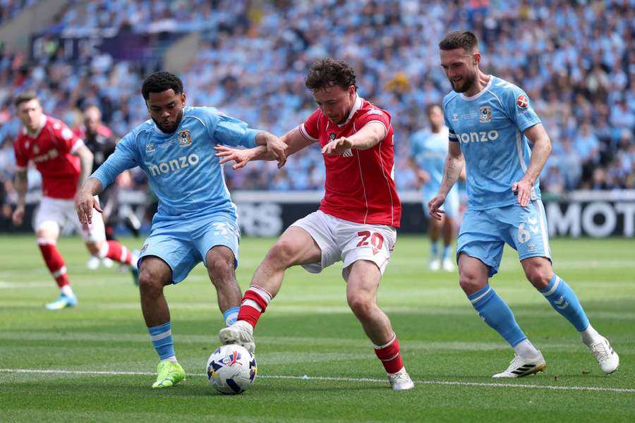 Oliver Rathbone of Wrexham is challenged by Jay Dasilva and Matt Grimes of Coventry