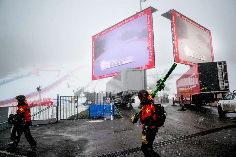 Skiers walk by giant screens announcing the cancellation of the men's Super-G event in Courchevel